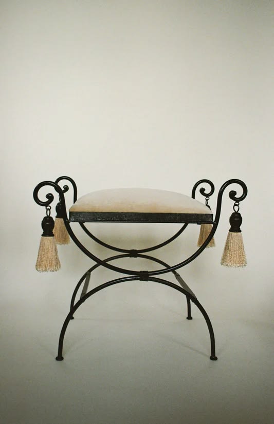 Wrought iron bench with scrolled arms and tasseled trim